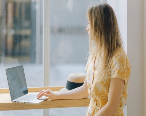 Woman taking a break from her laptop, looking out of a window in an urban office